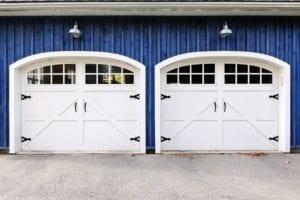 Two white carriage garage doors with windows on blue house