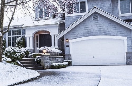 Suburban home with snow on drive way, lawn, plants, trees and roof